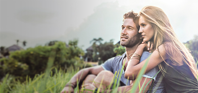 Ein junges Paar sitzt aneinander geschmiegt auf einer Wiese und blickt in die Ferne